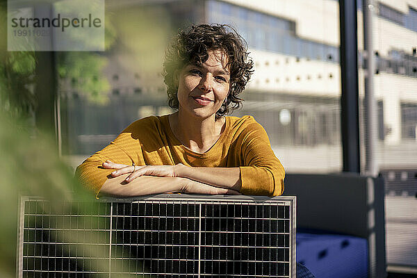 Lächelnde Geschäftsfrau sitzt mit Solarpanel im Büro