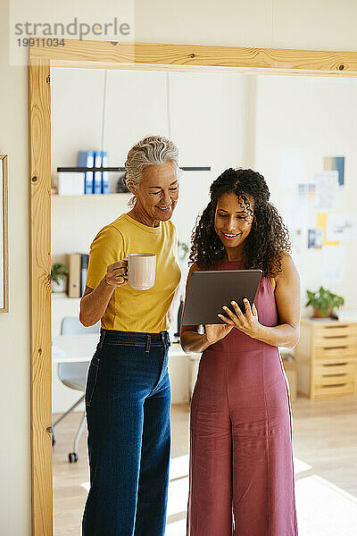 Lächelnde Geschäftsfrauen diskutieren mit Tablet-PC im Büro