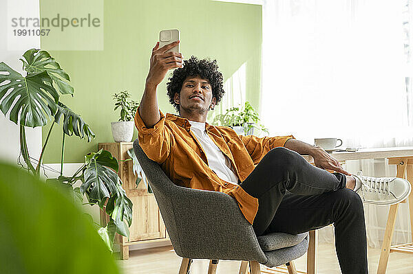 Geschäftsmann macht Selfie per Smartphone und sitzt auf einem Stuhl im Heimbüro