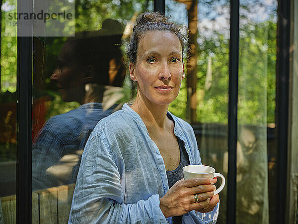 Frau mit Kaffeetasse vor dem Fenster