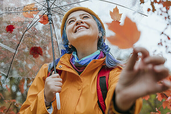 Lächelnde Frau mit Regenschirm und Blatt im Herbstpark