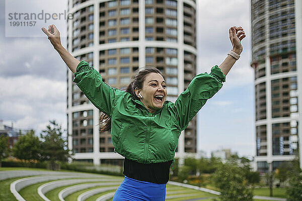 Beautiful woman exercises in a city park raising arms happily