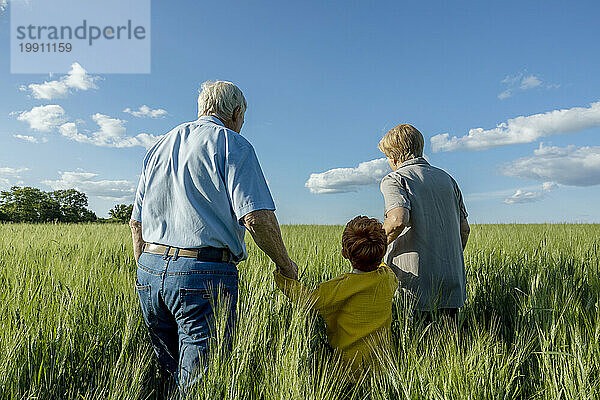 Älteres Paar hält die Hände seines Enkels  der auf dem Feld spaziert