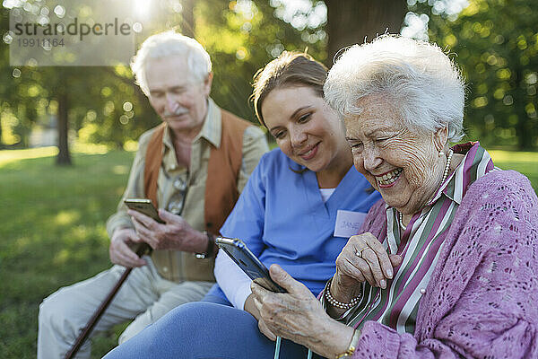 Glückliches Gesundheitspersonal mit älteren Männern und Frauen  die im Park ihr Smartphone nutzen