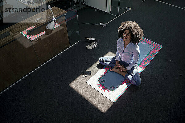 Businesswoman meditating on yoga mat at office