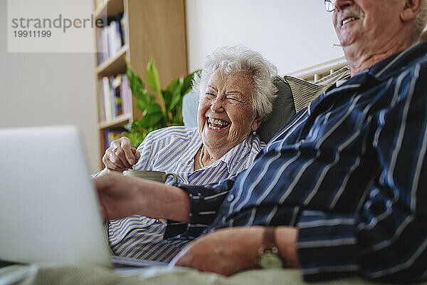 Fröhliches Seniorenpaar sitzt zu Hause mit Laptop