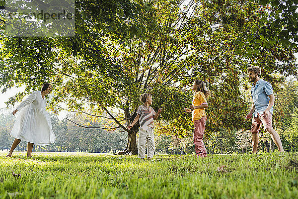 Vater und Mutter amüsieren sich mit Kindern in der Nähe eines Baumes im Park