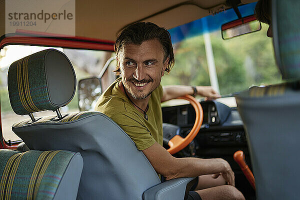 Smiling mature man sitting on driver's seat inside motor home