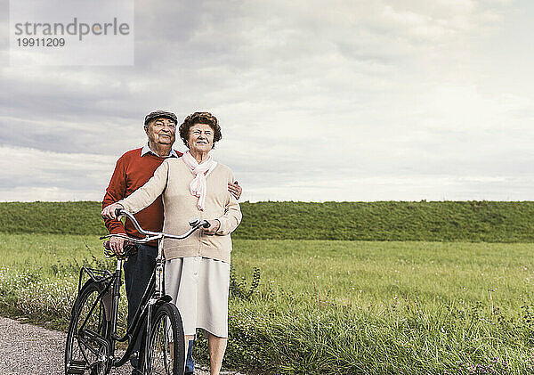Lächelndes älteres Paar steht mit Fahrrad auf Fußweg am Feld