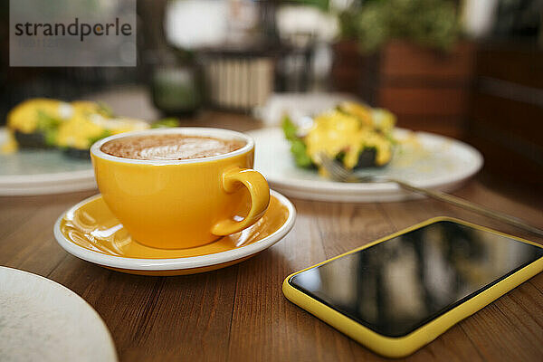 Gelbe Kaffeetasse mit Smartphone auf dem Tisch im Café