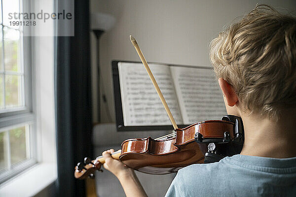 Junge übt zu Hause Geige mit Noten