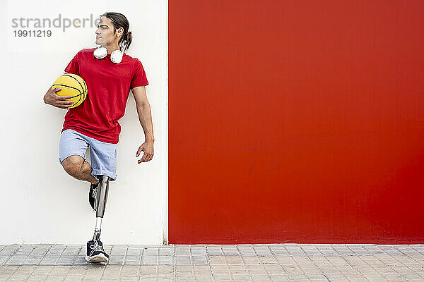 Mann mit Behinderung hält gelben Basketball in der Hand und lehnt an Wand