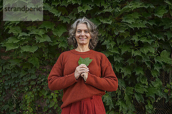 Reife Frau hält Blatt vor Pflanzen