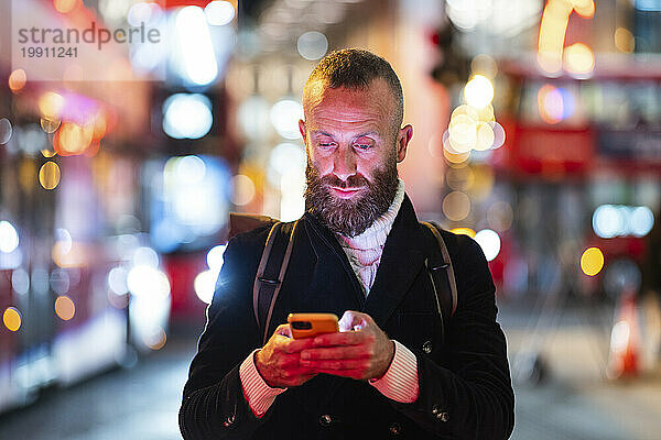 Mann benutzt nachts Smartphone in der Stadt