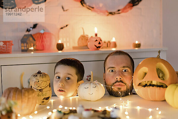 Vater und Sohn machen Mimik mit Kopf auf dem Tisch neben der Halloween-Dekoration zu Hause