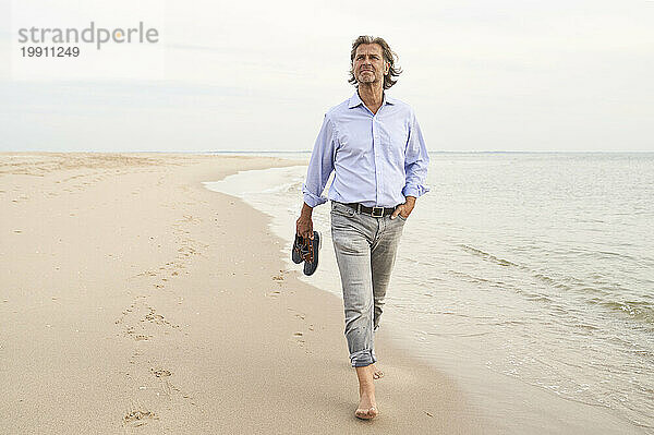 Mann hält Schuhe und läuft an der Küste am Strand entlang