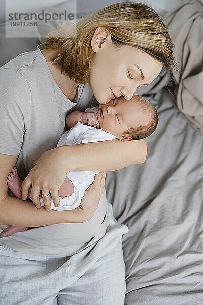 Liebevolle Mutter umarmt neugeborenen Sohn in den Armen
