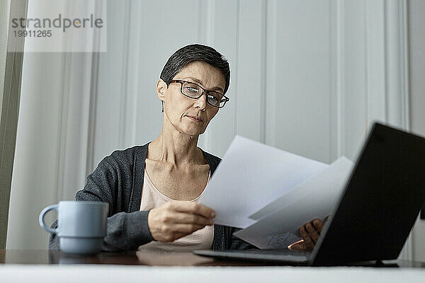 Erwachsene Frau arbeitet an einem Bericht und sitzt vor einem Laptop