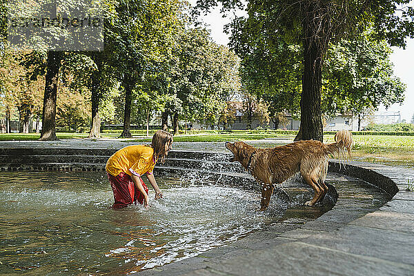 Mädchen spritzt Wasser auf Hund im Brunnen im Park