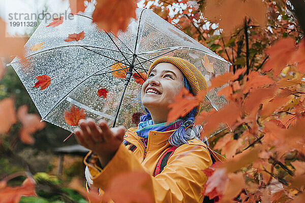 Glückliche Frau hält Regenschirm und genießt Regen im Herbstpark