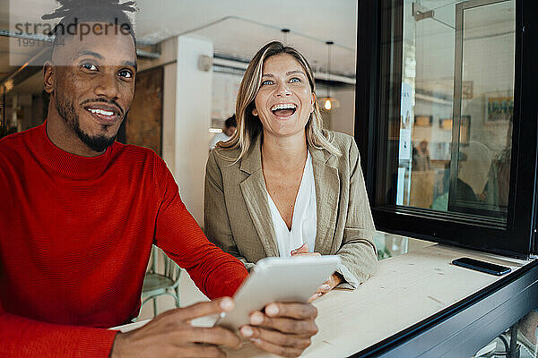 Laughing businesswoman sitting with colleague holding tablet PC at cafe
