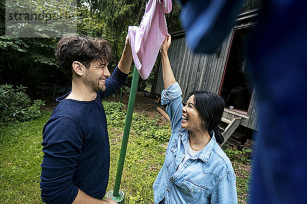 Glücklicher Mann und Frau halten rosafarbenes Tuch zum Trocknen vor der Blockhütte
