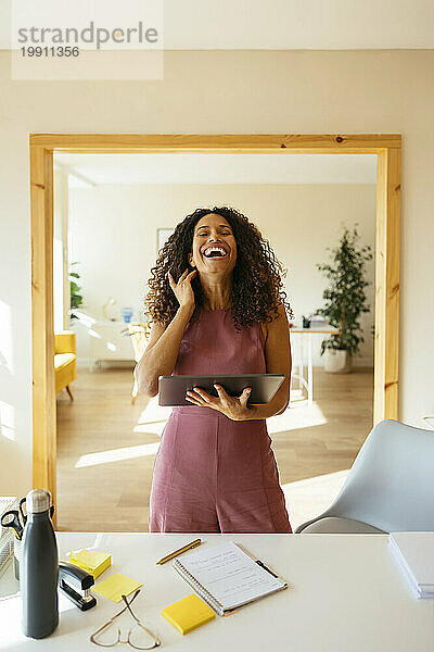 Glückliche Geschäftsfrau hält Tablet-PC in der Hand und lacht im Büro