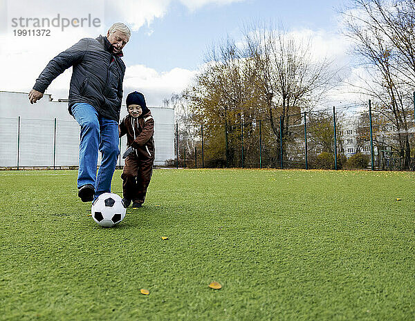 Enkel und Großvater haben Spaß beim Ballspielen auf dem Fußballplatz