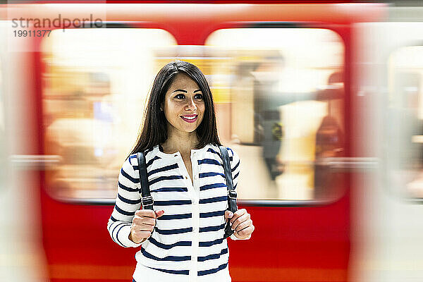 Glückliche Frau mit Rucksack steht vor der vorbeifahrenden U-Bahn