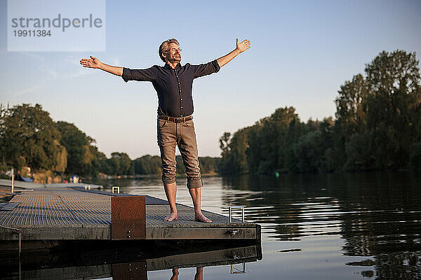 Senior man standing with arms outstretched on jetty