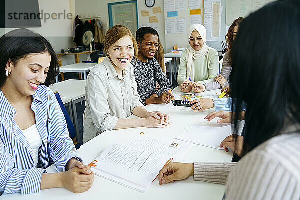 Lächelnde multiethnische Schüler lernen gemeinsam am Schreibtisch im Klassenzimmer