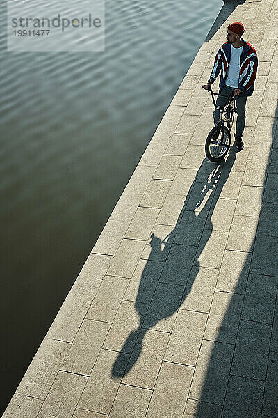 Man standing with BMX bike near lake on embankment