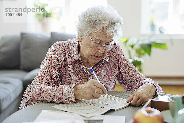 Ältere Frau mit Stift löst Kreuzworträtsel im Buch am Tisch