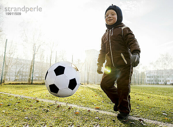 Lächelnder Junge  der mit Ball auf dem Fußballplatz spielt