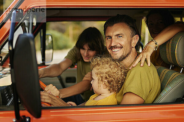 Glücklicher Mann mit Familie  der im Urlaub im Wohnmobil sitzt