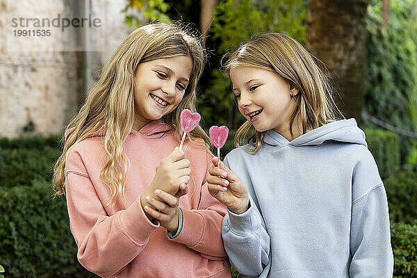 Glückliche Mädchen halten herzförmige Lutschbonbons im Park