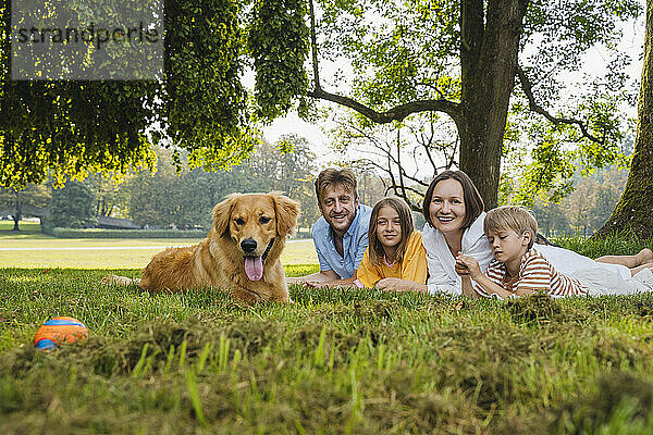 Glückliche Familie mit Hund  der im Park auf Gras liegt
