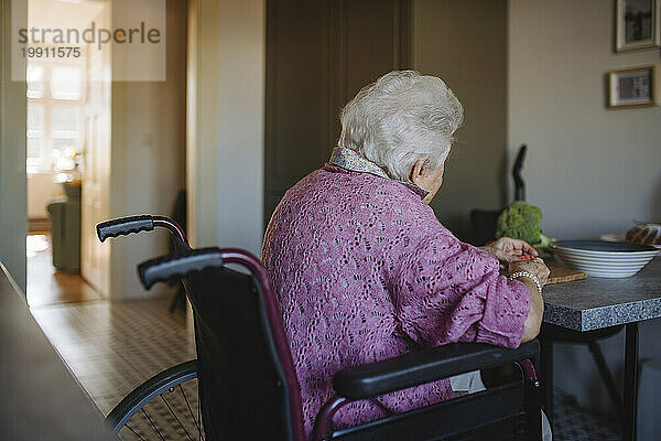 Ältere Frau sitzt im Rollstuhl am Tisch