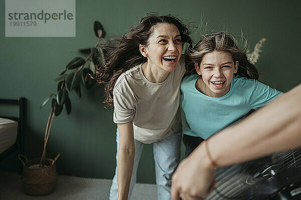 Mutter und Tochter amüsieren sich zu Hause mit elektrischem Ventilator