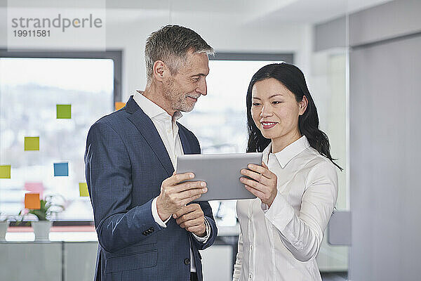 Lächelnde Geschäftsfrau diskutiert mit einem Kollegen im Büro über einen Tablet-PC