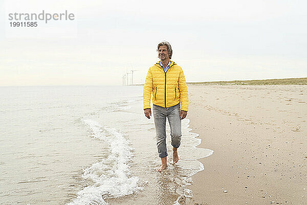 Älterer Mann trägt gelbe Jacke und geht am Strand spazieren