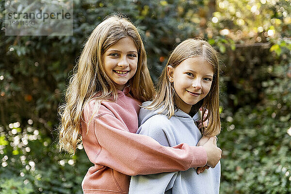 Happy girl standing with arm around friend in park