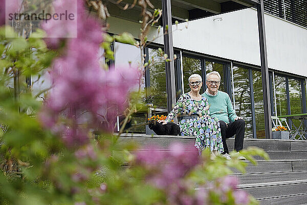 Glückliches Seniorenpaar sitzt auf Stufen vor seinem Haus