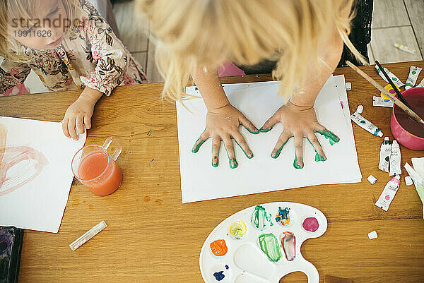 Girl making handprint with watercolors on paper at home