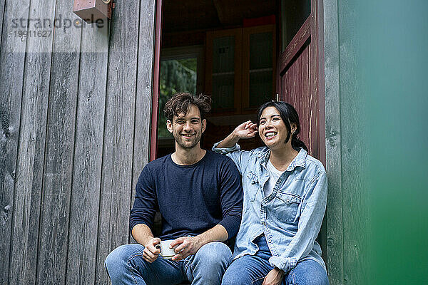 Glücklicher Mann und Frau sitzen in der Tür einer Blockhütte