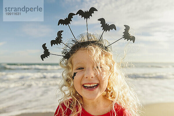 Fröhliches Mädchen mit Halloween-Stirnband und Fledermäusen am Strand