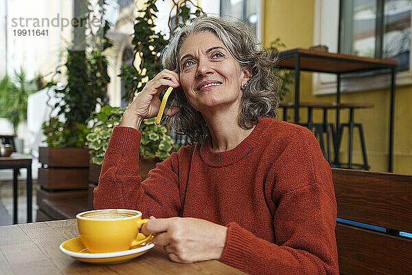 Lächelnde reife Frau  die im Straßencafé mit dem Smartphone spricht