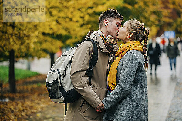 Romantische Frau küsst Freund mit Rucksack auf der Straße