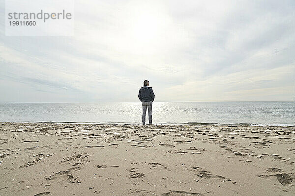 Mann steht am Strand vor dem Meer