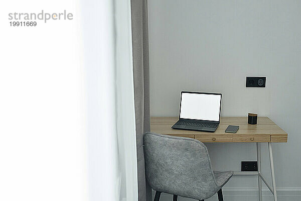 Holztisch mit kabellosem Laptop darauf im Heimbüro